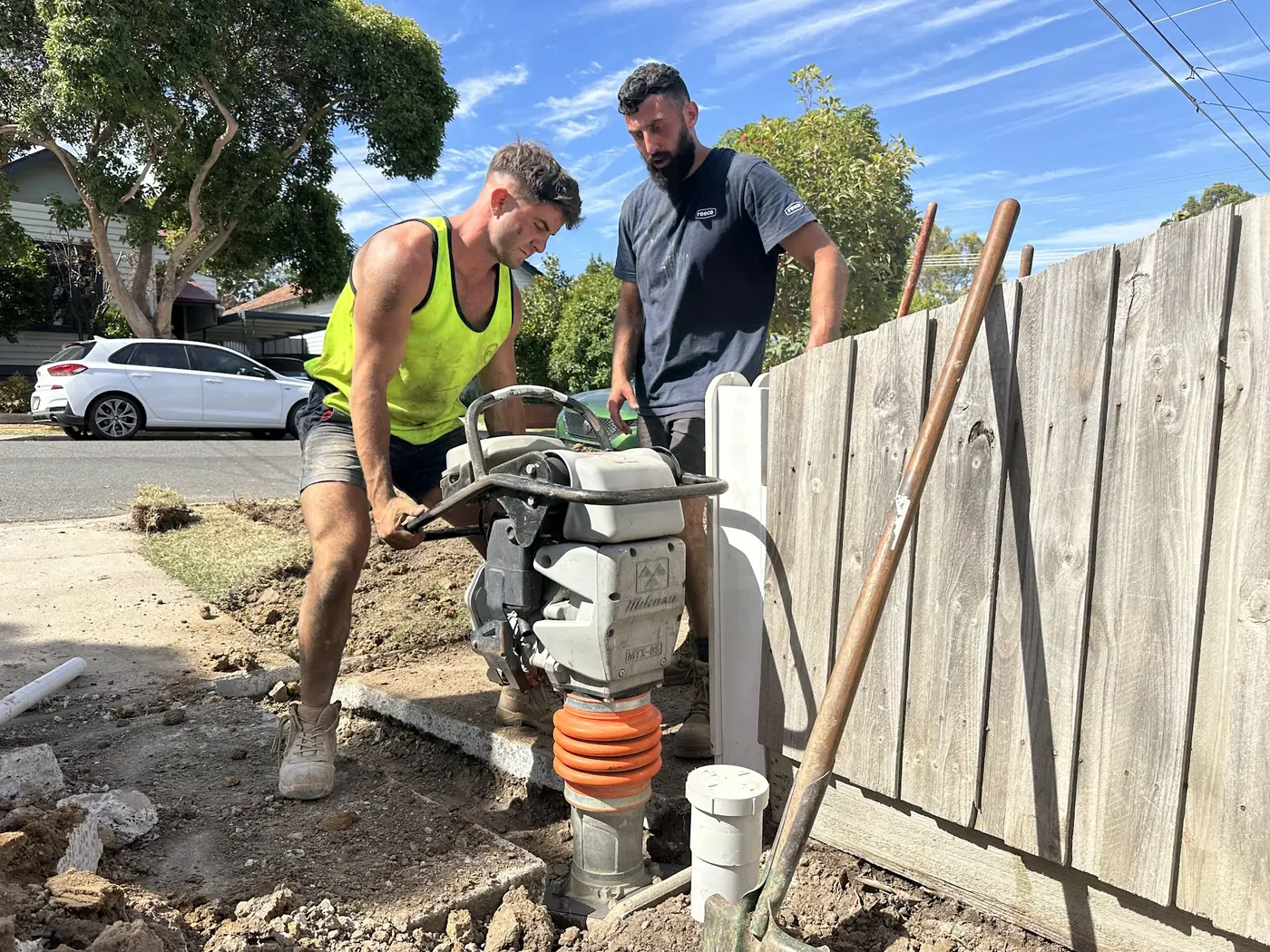 Aquaflex team compacting a filled trench beside a fence